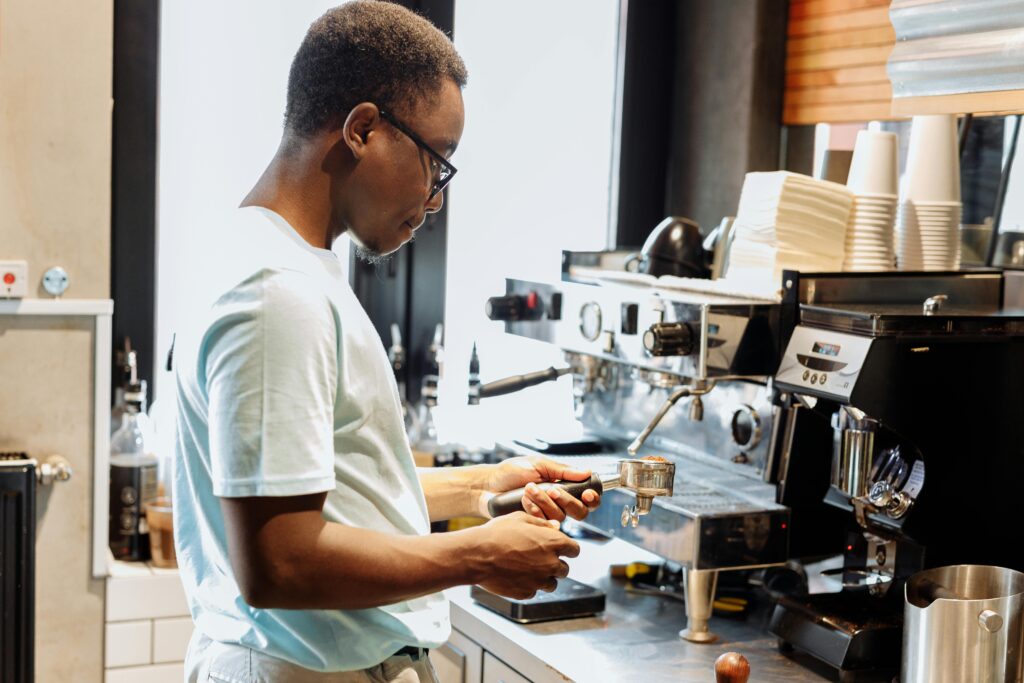 A barista is making coffee using an espresso machine in a lively cafe setting.