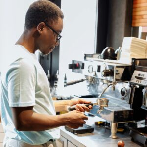 A barista is making coffee using an espresso machine in a lively cafe setting.
